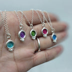 cinco colgantes de plata con esmalte de color agua, morado, verde, fucsia y azul, de la colección bubble, expuestos sobre una mano. foto detalle